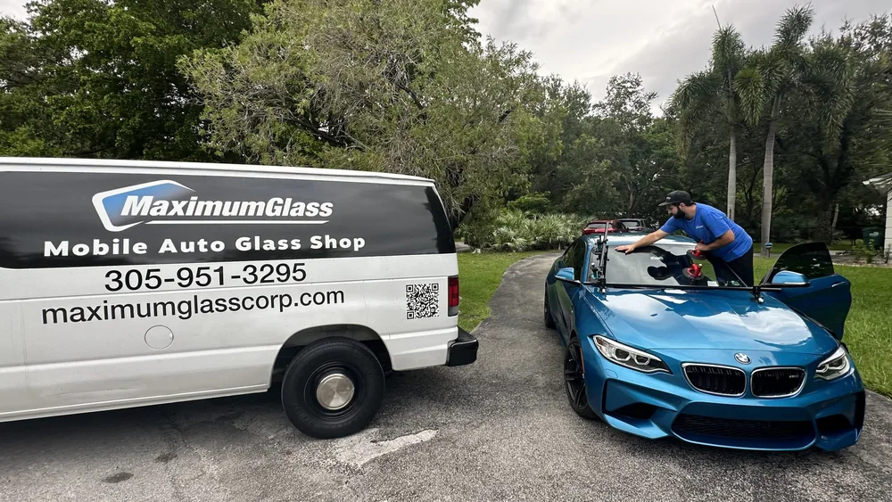 Technician pressing a new windshield into place with suction cups on a blue BMW