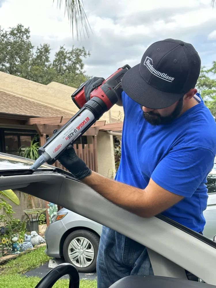 Technician running a urethane bead along the windshield aperture with a powered gun